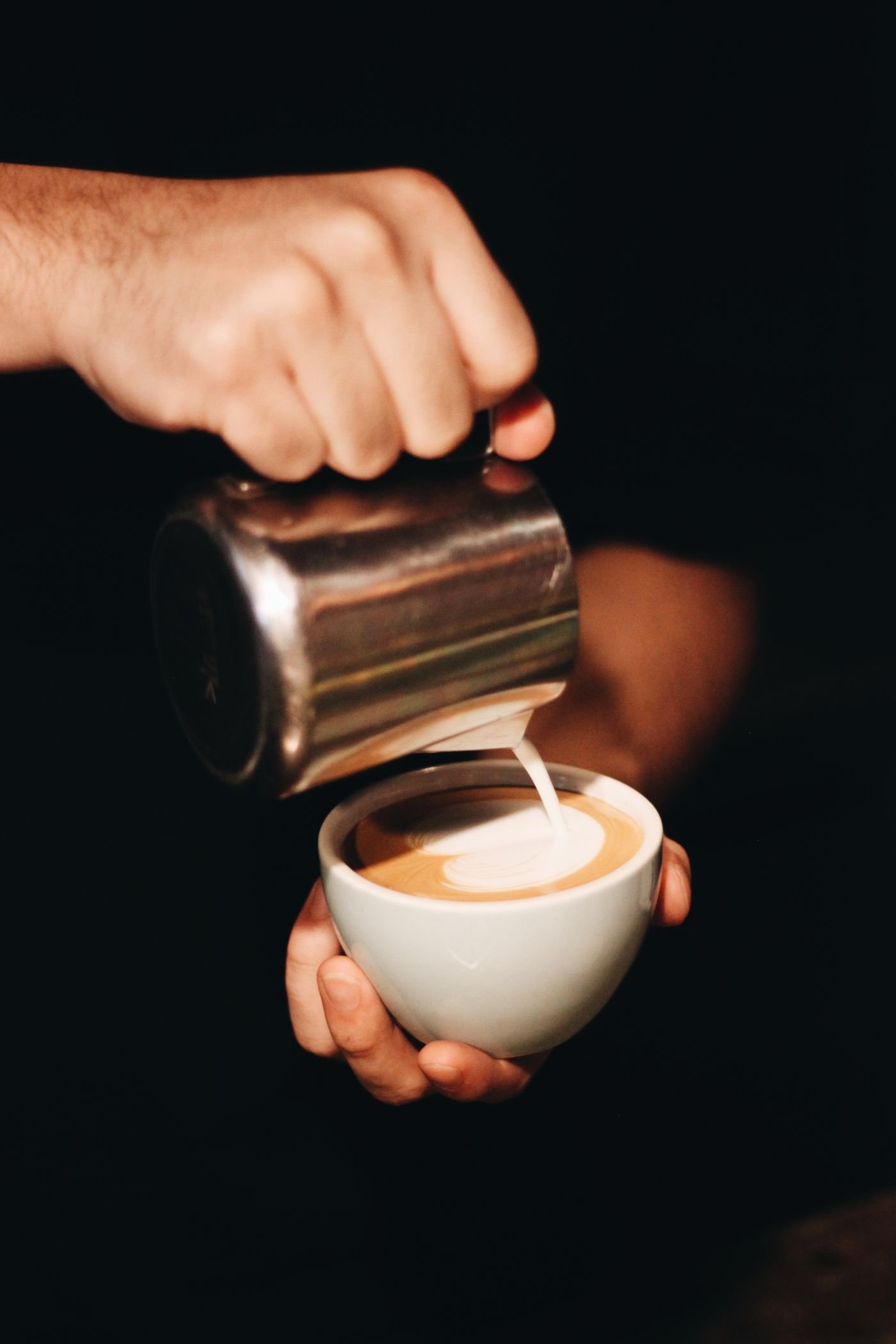 Barista pouring milk to finish a cup of coffee